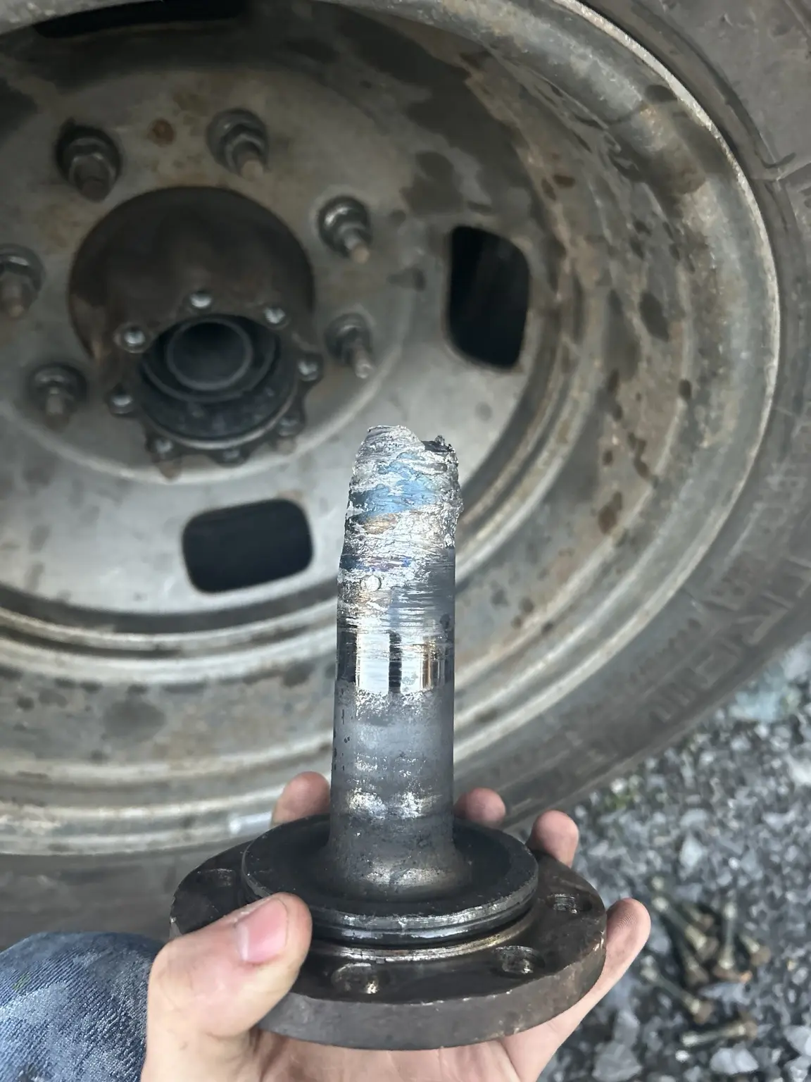 Broken rear axle held in front of a wheel after an unaddressed blown hub seal caused the axle to break in half.