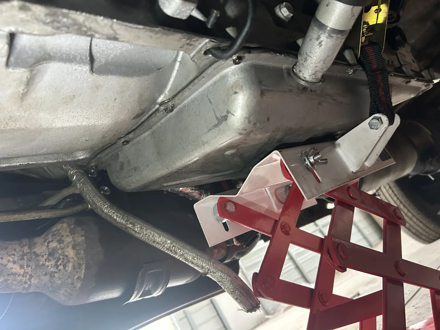 Underside of a vehicle with a transmission jack in position during a transmission swap.